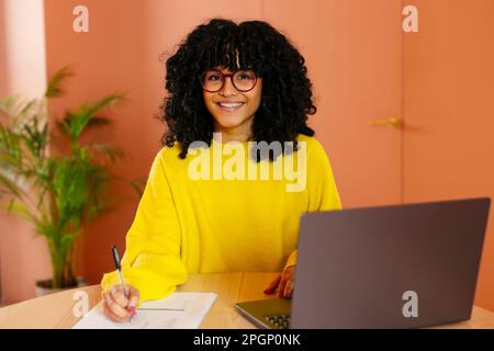 Jeune femme confiante assise au bureau avec un ordinateur portable au bureau Banque D'Images