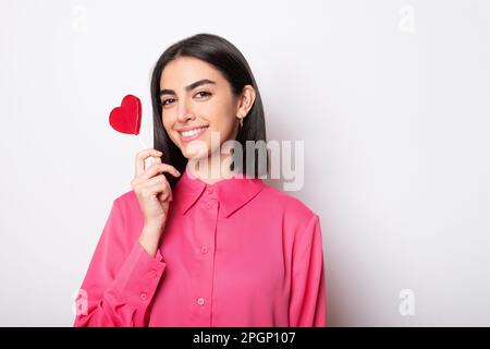Bonne jeune femme tenant un lollipop en forme de coeur rouge sur fond blanc Banque D'Images