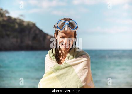 Femme souriante enveloppée dans une couverture portant des lunettes de plongée Banque D'Images