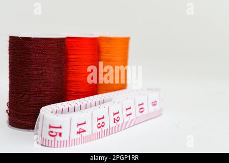prend environ trois bobines de fil orange de différentes nuances et une mesure de ruban blanc avec des nombres rouges sur un fond blanc. Banque D'Images