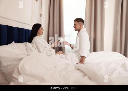 Couple heureux portant des peignoirs reposant sur le lit dans la chambre d'hôtel Banque D'Images