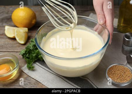 Femme faisant de la mayonnaise maison dans un bol en verre à table en bois, gros plan Banque D'Images