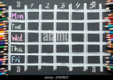 Crayons colorés et horaires hebdomadaires dessinés sur tableau noir, vue du dessus Banque D'Images