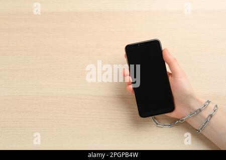 Dépendance à l'Internet. Vue de dessus d'une femme tenant un smartphone sur une table en bois, chaînée à la main à l'appareil Banque D'Images