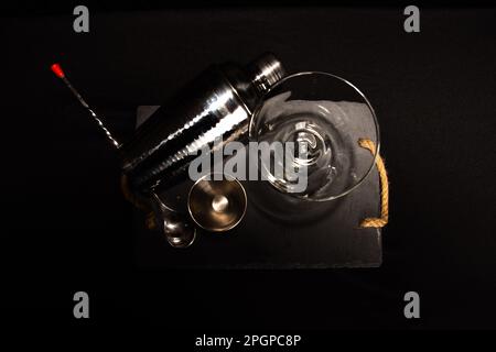 Instruments de cocktail sur fond noir. Jigger, shaker, cuillère et verre martini. Vue sur le Zénith. Banque D'Images