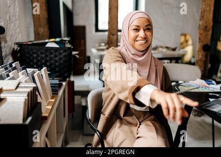 Une femme arabe joyeuse, portant le doigt de la hijab pendant qu'elle est assise à l'atelier Banque D'Images