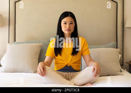 Portrait d'une femme asiatique assise à pieds croisés sur le lit méditant. Un style de vie sain, du temps libre et de la détente. Banque D'Images