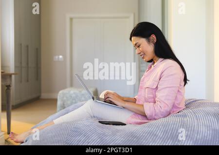 Une femme asiatique heureuse assise sur un sac à dos avec un ordinateur portable, souriante. Style de vie, temps libre, communication et détente. Banque D'Images
