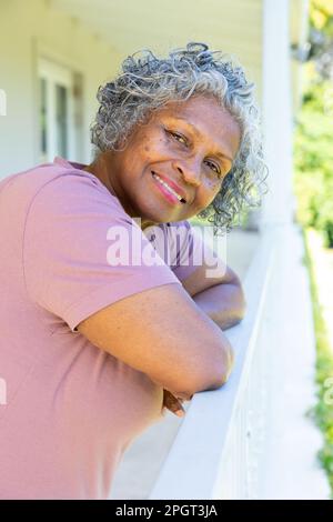 Gros plan sur une femme senior afro-américaine souriante aux cheveux gris courts, agenouillée sur une main courante sur le balcon. Non modifié, style de vie, retraite, portrait, bras Banque D'Images