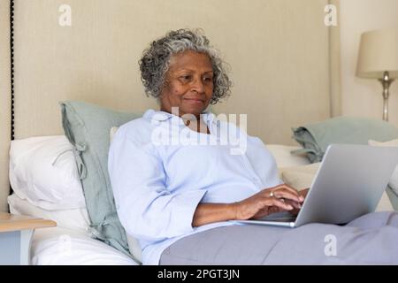 Femme d'affaires afro-américaine concentrée travaillant sur un ordinateur portable tout en étant assise sur un lit, un espace de copie. Non modifié, professionnel, travail à la maison, Internet Banque D'Images