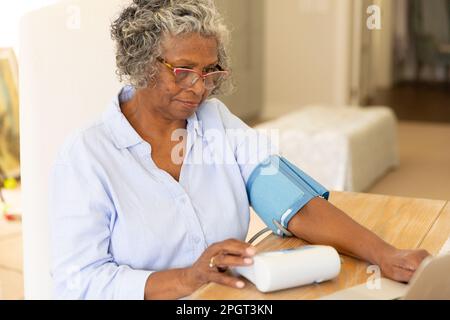 Femme afro-américaine âgée examinant sa tension artérielle avec un manomètre sur table à la maison, espace de copie. Non modifié, style de vie, médical, soins de santé, eyeglas Banque D'Images