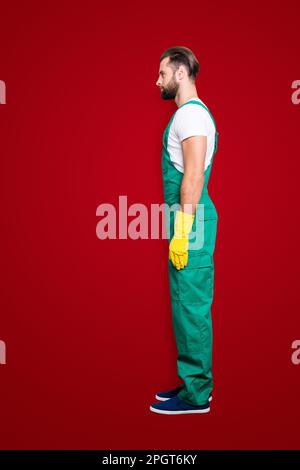 Vue latérale demi-visage à pression, portrait plein corps de virile dur barbu homme concentré avec le chaume, coiffure en uniforme vert, isolé sur Banque D'Images