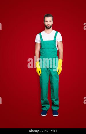 Portrait complet de la belle femme de ménage concentrée barbu avec barbe de 3 jours, coiffure en uniforme vert, isolée sur gris Banque D'Images