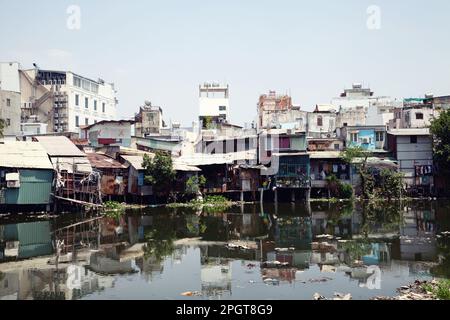 Vieilles maisons sur pilotis dans les bidonvilles de Saigon le long d'une rivière pleine de déchets. Quartier résidentiel pauvre à Ho Chi Minh ville, Vietnam, debout sur l'eau Banque D'Images