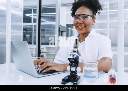 sourire noir scientifique médecin étudiant étudiant et d'expérience analyse échantillon de test avec l'écriture rapport dans l'ordinateur. SPE ambitieuse jeune biotechnologie Banque D'Images