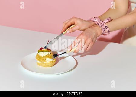 Coupe courte des mains liées de la femme modèle avec du ruban de mesure prenant le gâteau sur fond rose. Gros plan Banque D'Images