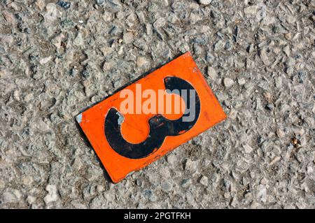 Numéro 3 sur une plaque métallique orange, posée sur le sol. Banque D'Images
