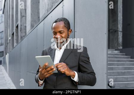 Homme d'affaires noir debout près du centre de bureau et travaillant sur une tablette. Banque D'Images