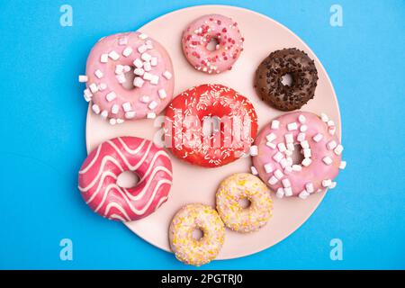 Plusieurs beignets différents sur fond bleu vue du dessus, des beignets roses, blancs et chocolat Banque D'Images