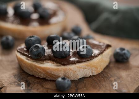 Tartinade au chocolat et aux noisettes bio avec des bleuets frais sur des tranches de ciabatta sur une planche de bois, foyer peu profond Banque D'Images