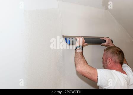 Un homme applique du plâtre polymère prêt à l'emploi à partir d'un seau à l'aide de pinces à plâtre spéciales. Banque D'Images