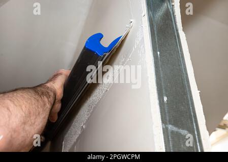 Un homme applique du plâtre polymère prêt à l'emploi à partir d'un seau à l'aide de pinces à plâtre spéciales. Banque D'Images