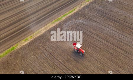 Vue ci-dessus sur le tracteur comme des lancers, fertilisant les terres arables pour de nouvelles récoltes, traînant la machine agricole montée pour l'épandage d'engrais artificiel. Banque D'Images