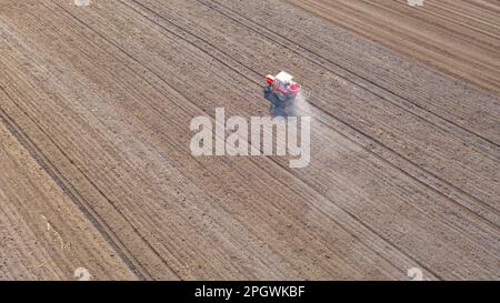 Vue ci-dessus sur le tracteur comme des lancers, fertilisant les terres arables pour de nouvelles récoltes, traînant la machine agricole montée pour l'épandage d'engrais artificiel. Banque D'Images