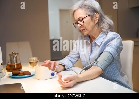 Une femme âgée inquiète mesure sa tension artérielle avec un tonomètre Banque D'Images