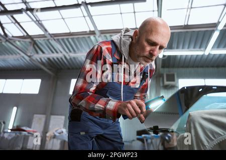 Homme dans les vêtements de travail travaille avec un détail de voiture Banque D'Images