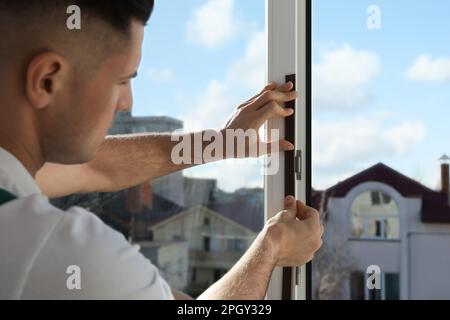 Homme mettant la bande de traction en caoutchouc sur la fenêtre à l'intérieur, se concentrer sur les mains Banque D'Images