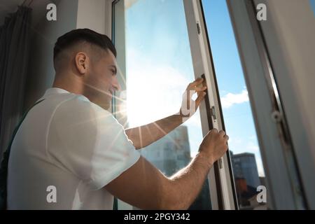 Homme posant une bande de traction en caoutchouc sur la fenêtre à l'intérieur Banque D'Images