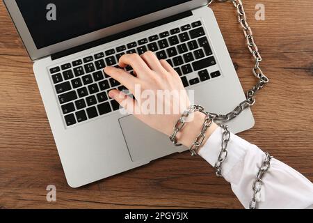 Femme avec clavier en chaîne sur ordinateur portable à table en bois, vue de dessus. Dépendance à l'Internet Banque D'Images