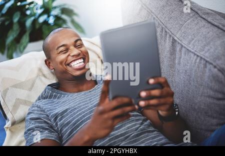 Il n'est pas nécessaire de quitter la maison pour se divertir. un beau jeune homme utilisant une tablette numérique à la maison. Banque D'Images