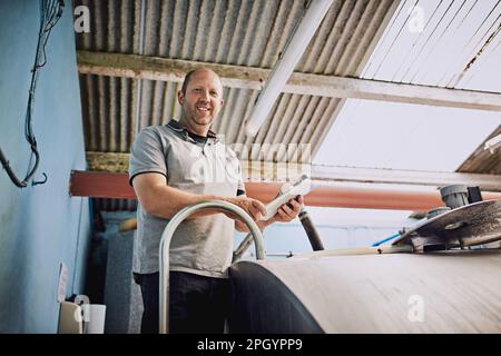 Assurez-vous que le lait est correctement traité. Portrait à angle bas d'un fermier mâle remplissant des récipients à lait dans son usine laitière. Banque D'Images