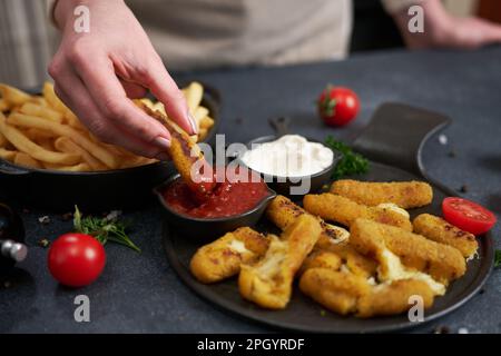 La femme trempette le bâton de mozzarella au fromage dans la sauce trempée Banque D'Images