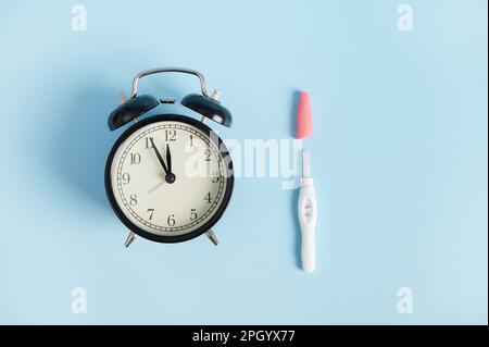 Réveil à vie fixe et kit de test de grossesse à jet d'encre positif avec deux bandes sur fond bleu. Concept de maternité Banque D'Images