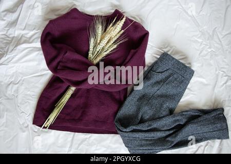 le chandail en laine rouge pour femmes et le pantalon gris avec un bouquet d'épillets de blé se trouvent sur un fond clair et rusé Banque D'Images