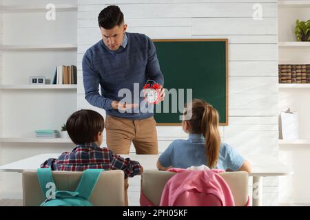 Professeur avec un réveil qui fait entrer les élèves en retard dans la salle de classe Banque D'Images