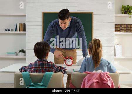 Professeur avec un réveil qui fait entrer les élèves en retard dans la salle de classe Banque D'Images