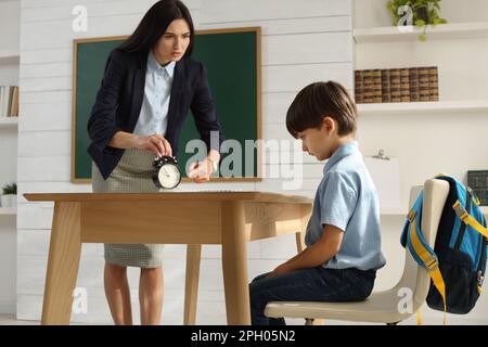 Professeur avec un réveil, un élève qui se colte pour être en retard dans la classe Banque D'Images