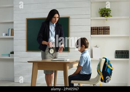 Professeur avec un réveil, un élève qui se colte pour être en retard dans la classe Banque D'Images