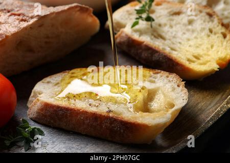 Verser de l'huile sur des tranches de pain sur une assiette en bois, gros plan Banque D'Images