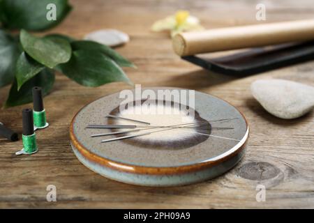 Dessous de verre en pierre grise avec aiguilles d'acupuncture sur une table en bois Banque D'Images