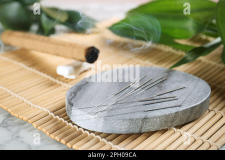 Dessous de verre en pierre grise avec aiguilles d'acupuncture sur un tapis en bambou Banque D'Images