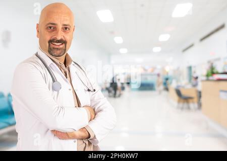 Médecin de confiance, portrait d'un homme d'âge moyen fier médecin de confiance. Bras croisés à l'hôpital. Arrière-plan abstrait flou du centre médical. Banque D'Images