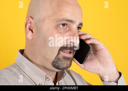 Portrait d'un homme d'âge moyen parlant sur un téléphone portable. Chauve, barbu, homme du Caucase du millénaire tenant un smartphone moderne. Banque D'Images