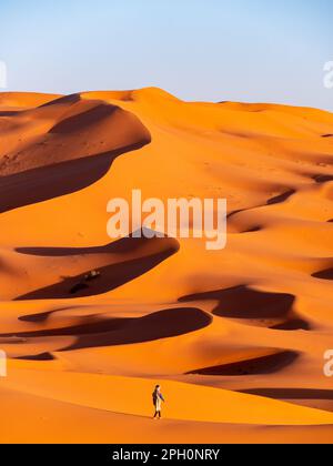 Berber homme marchant parmi les dunes de sable au loin, près de Merzouga, Maroc pendant le coucher du soleil Banque D'Images