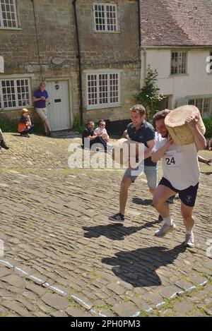 Les concurrents de la course du fromage masculin portent leurs fromages sur Gold Hill, Shaftesbury, lors du festival de la gastronomie et des boissons de la ville, le 8th mai 2022. Banque D'Images