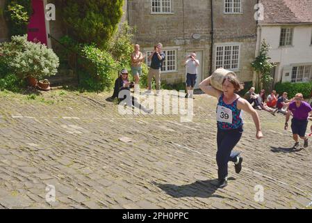 Les concurrents de la course de fromages Ladies portent leurs fromages sur Gold Hill, Shaftesbury, lors du festival de la gastronomie et des boissons de la ville, le 8th mai 2022. Banque D'Images